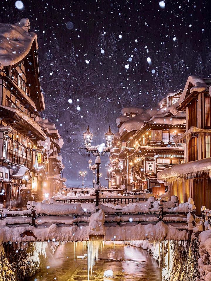 Nostalgic street in Ginzan Onsen illuminated by kerosene lamps with traditional wooden buildings and a snowy winter landscape