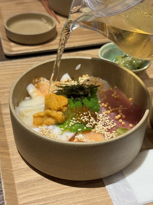 Hot broth being poured over seafood ochazuke at Kyoto Obuya, a must-visit restaurant near Kyoto Station, enhancing the flavors of the fresh ingredients.