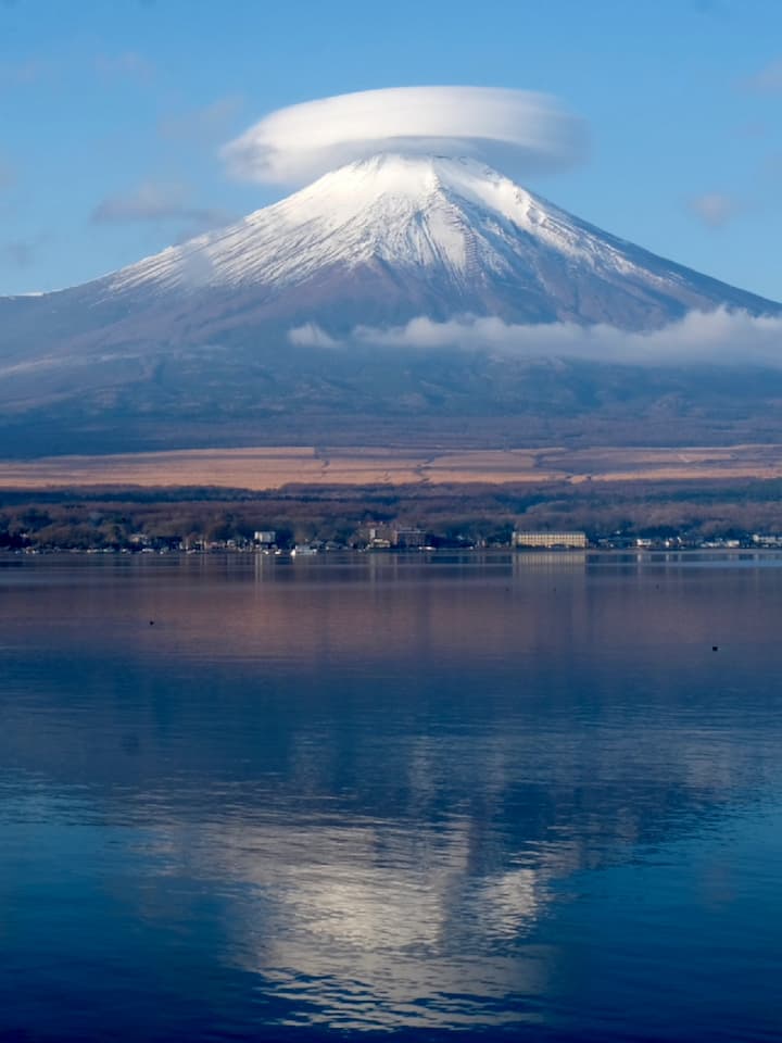 Serene view of Lake Yamanaka before sunrise with Mount Fuji in the background, featuring a unique cloud formation over the mountain